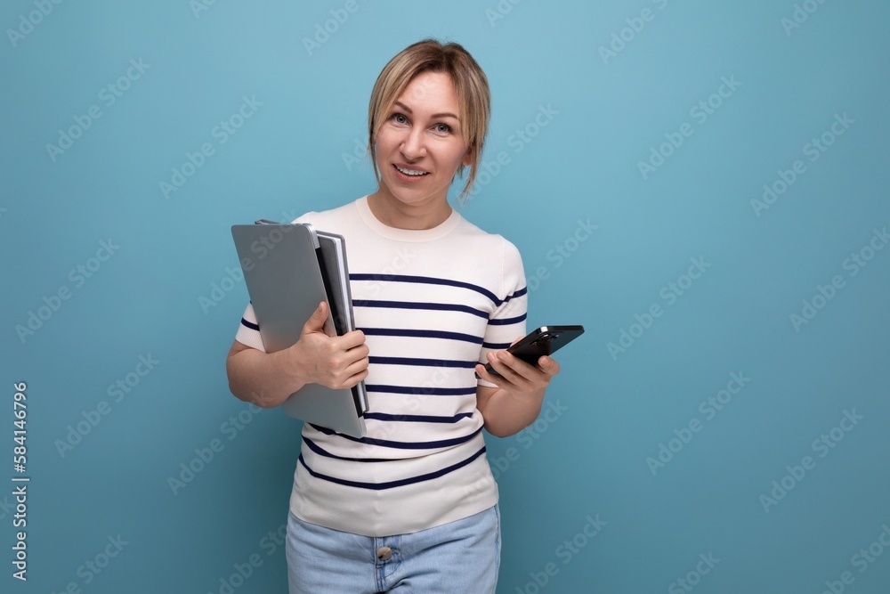 close up photo of smart blond female student in casual outfit with laptop and notepad on blue background with copy space close up photo of smart blond female student in casual outfit with laptop and notepad on blue background with copy space