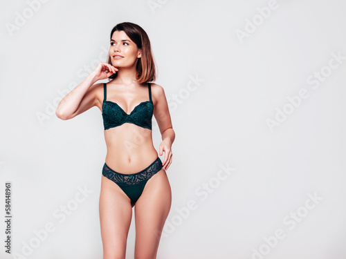 Young beautiful sexy woman in green lace lingerie. Smiling carefree confident model wearing green underwear. Hot brunette posing on white wall in studio. Perfect body. Slim and fit. Isolated © halayalex
