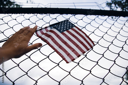 Hand holding america flag in front of a barbed fence. Illegal immigration concept. photo