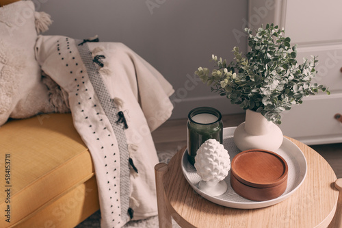 cozy spring home details. House plant, candle and decorations composition on coffee table with chair on background.