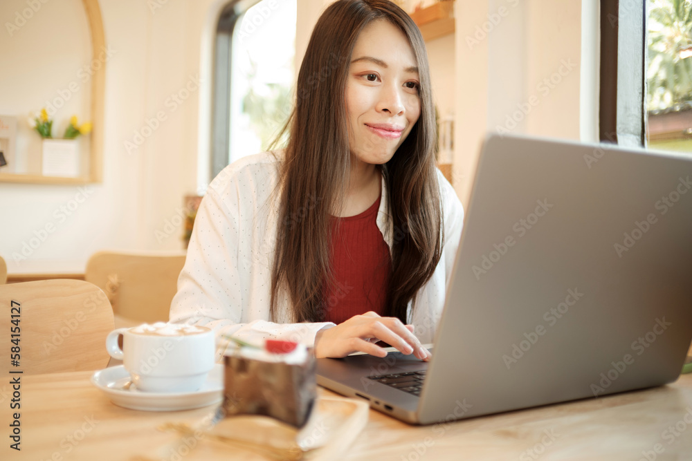 An Asian businesswoman is working on her laptop while drinking hot coffee in a cafe. An Asian businesswoman is working on her laptop while drinking hot coffee in a cafe.