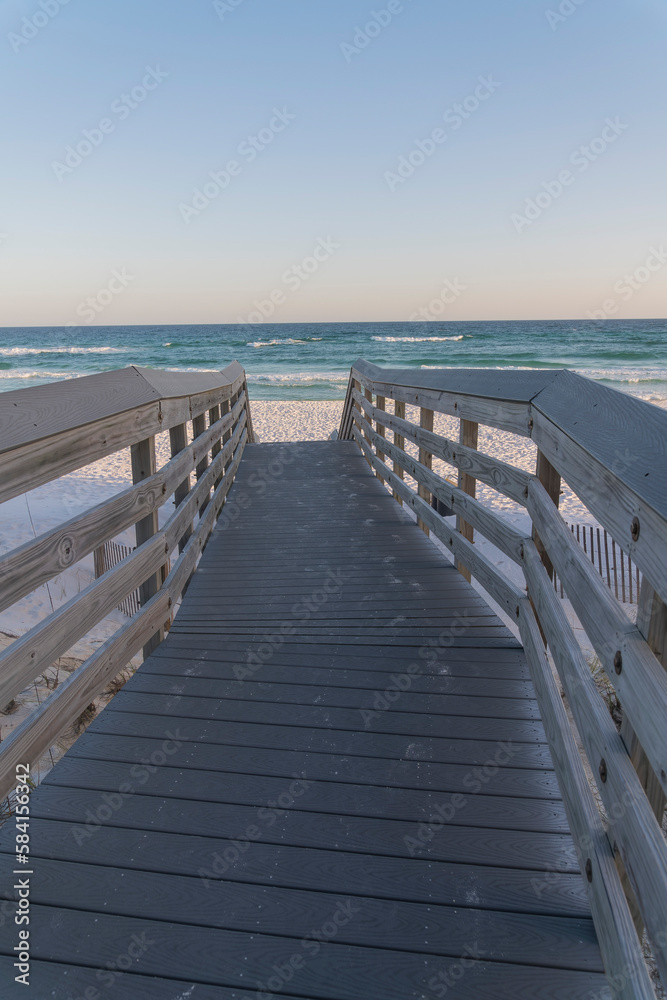 Wooden sloped walkway with railings heading to the beach with white sand in Destin, Florida. Seascape with horizon skyline view from a boardwalk.