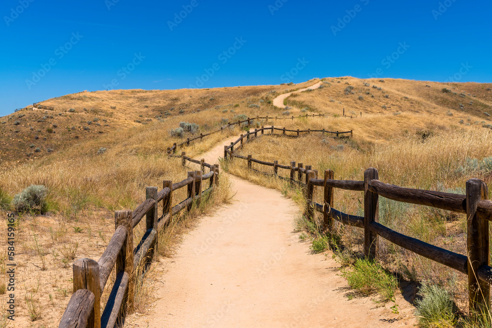Boise, Idaho- Flattened trail with wooden barriers on a mountain. Mountain trail in the middle of grassland of a mountain slope against the clear blue sky.