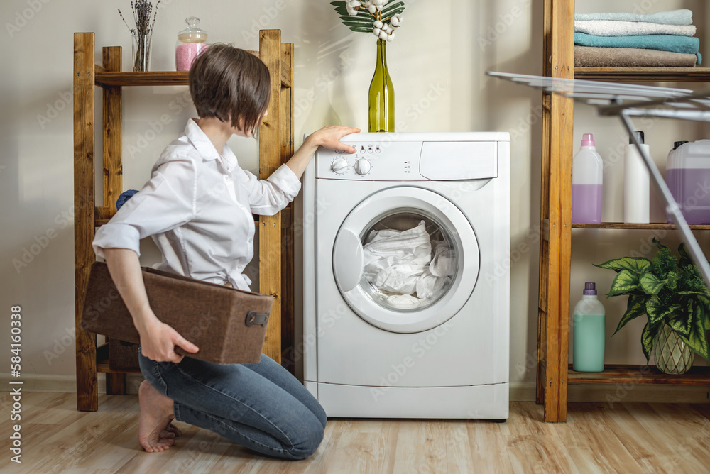 Woman is washing clothes in a washing machine in a laundry room. The concept of caring for things, cleaning and hygiene Woman is washing clothes in a washing machine in a laundry room. The concept of caring for things, cleaning and hygiene