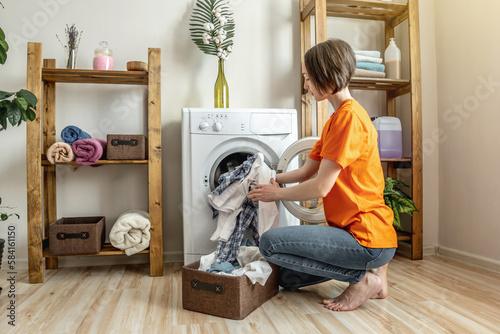 Woman is puting multicolor clothes into the washing machine in the laundry room. The concept of caring for things, cleaning and hygiene