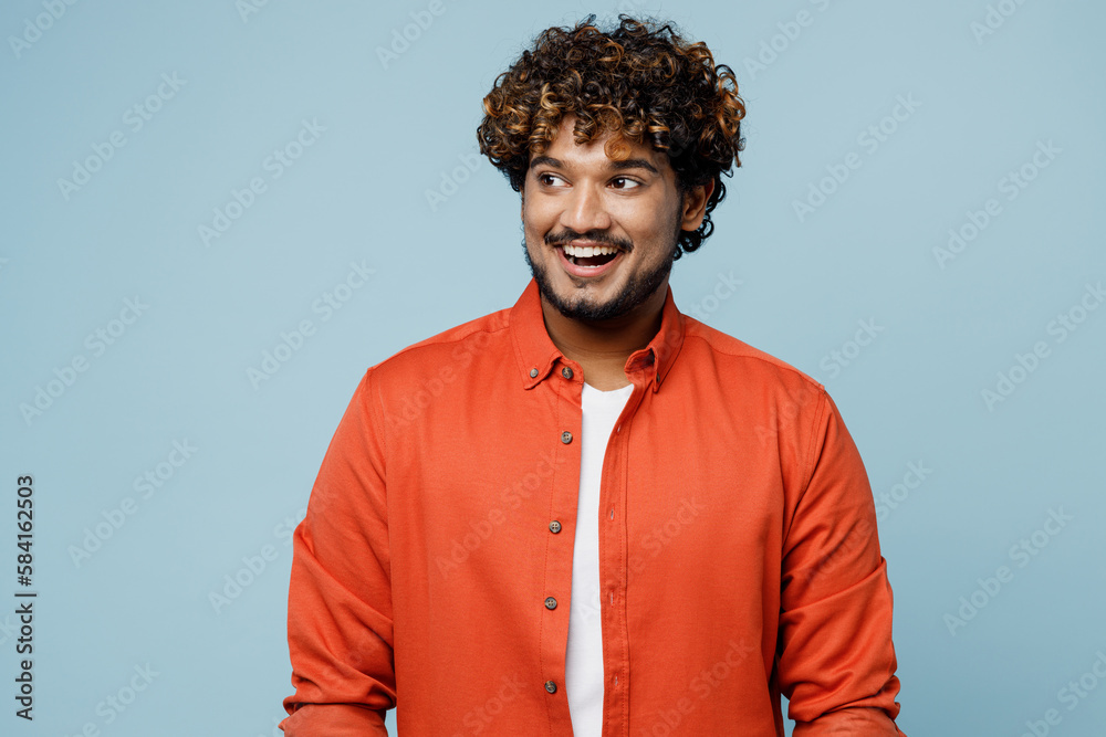 Fototapeta premium Young smiling happy fun cheerful Indian man wearing orange red shirt white t-shirt look aside on workspace area isolated on plain pastel light blue cyan background studio portrait. Lifestyle concept.