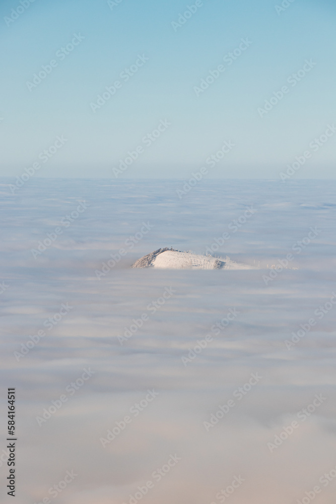 Fototapeta premium View of the top of Mount Skalka in the Beskydy Mountains under the cover of thick white fog in the morning hours. Snowy hills with clouds. Being above the clouds