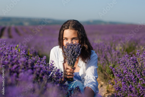 A beautiful teenage girl in a light-coloured shirt and blue skirt amongst flowers in a lavender field.