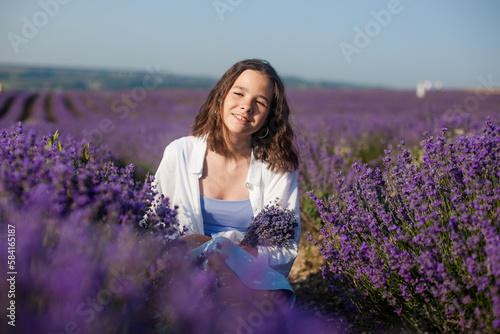 A beautiful teenage girl in a light-coloured shirt and blue skirt amongst flowers in a lavender field.