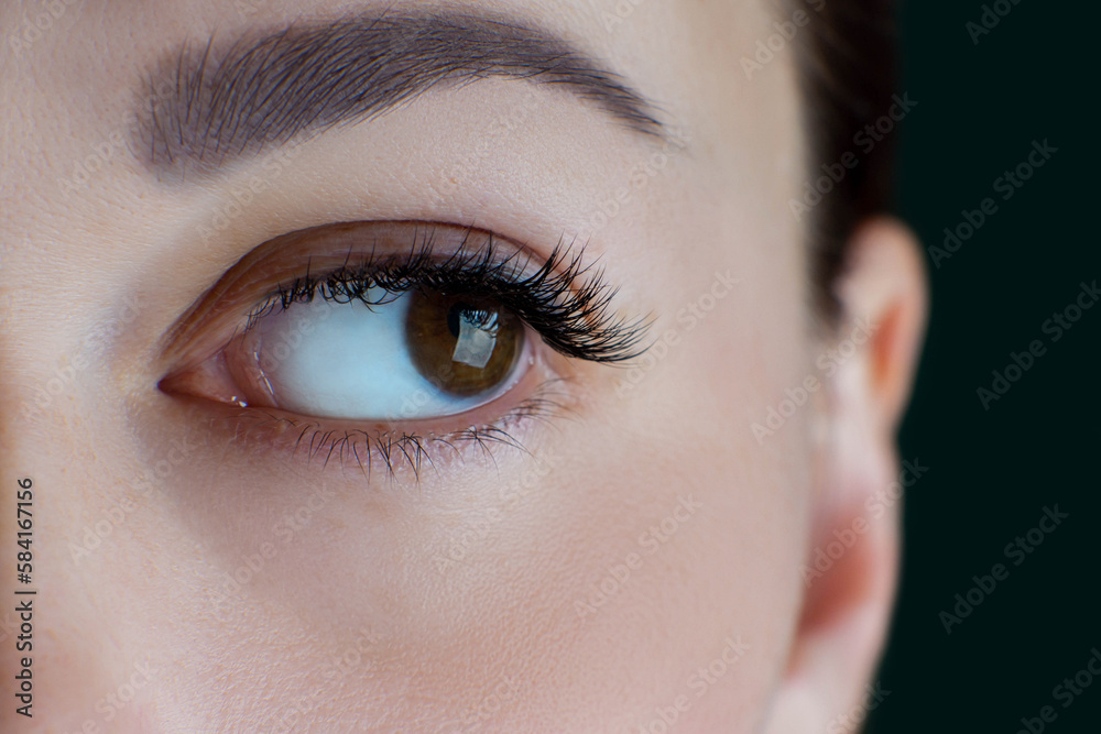 Close-up of brown eye with extreme long eyelashes, black eyeliner, healthy skin, flawless eyebrow of unrecognizable young woman looking aside. Macro. Eyelash extension, beauty procedures, cosmetology.
