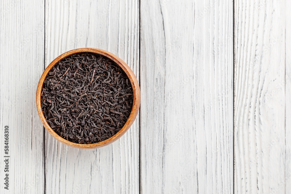 Dry black tea in wooden bowl on white wooden background with copy space