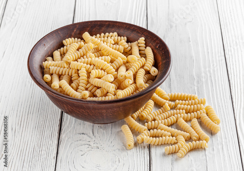 Obraz na płótnie Uncooked fusilli pasta in ceramic bowl on white wooden background w salonie