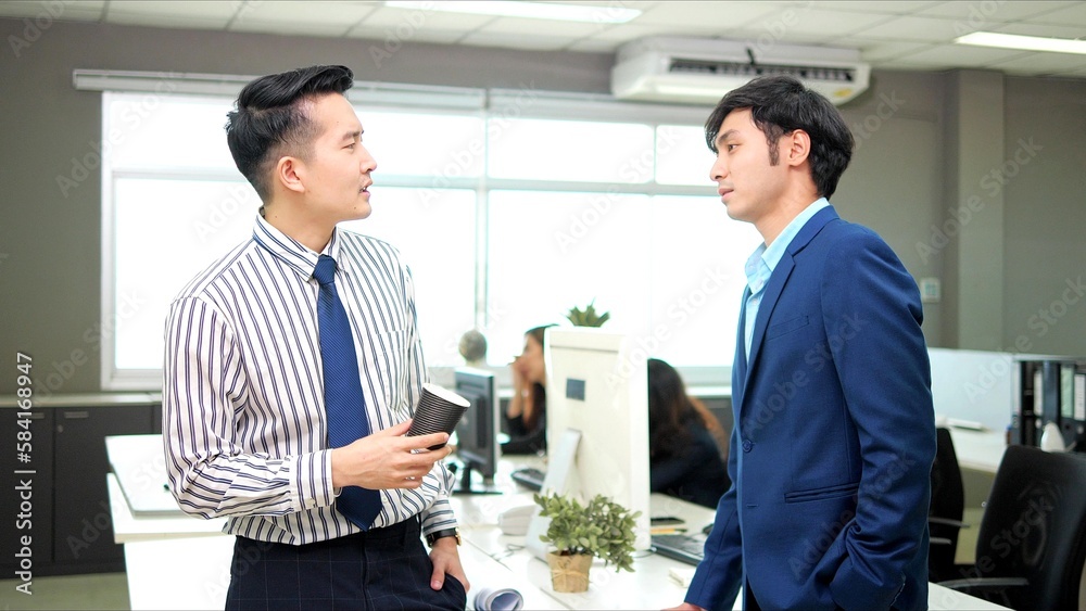 Two male colleagues employees cooperating in office talking working together at workplace, smiling and drinking coffee Two male colleagues employees cooperating in office talking working together at workplace, smiling and drinking coffee