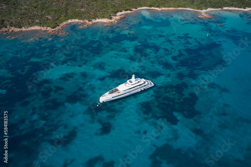 Large white yacht along the coastline at anchor. Large white modern mega yacht on transparent blue water, anchorage top view. © Berg