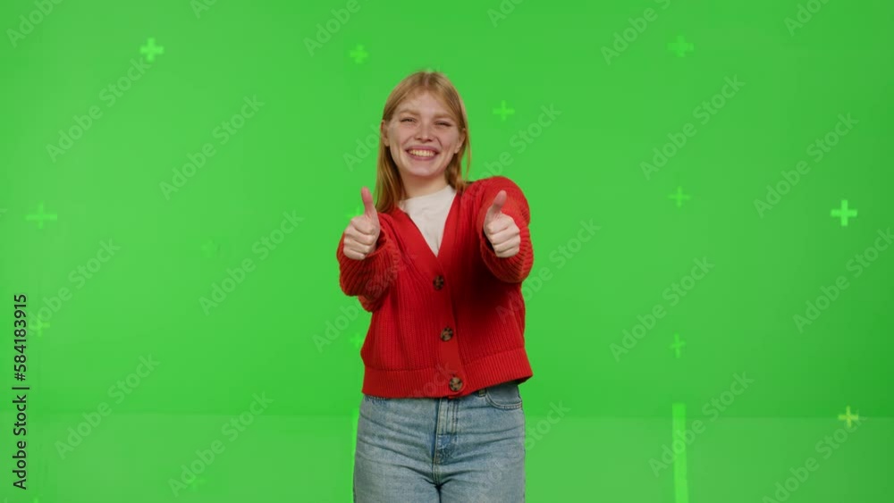 Attractive blond redhead girl showing thumbs up on green screen background. Happy young woman in jeans and a knitted jumper in a positive mood approving Attractive blond redhead girl showing thumbs up on green screen background. Happy young woman in jeans and a knitted jumper in a positive mood approving