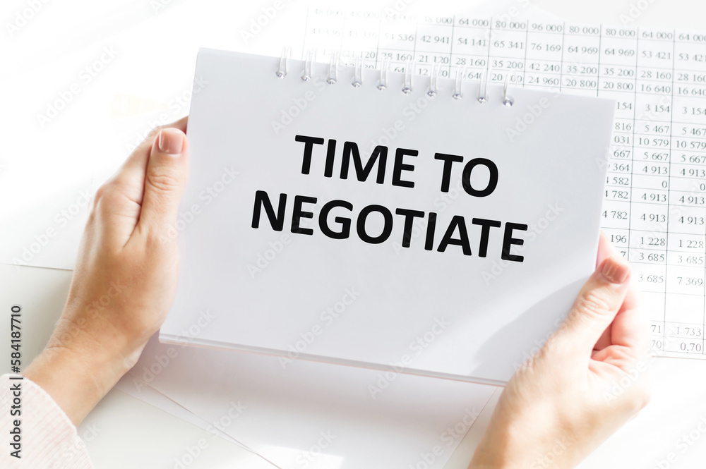 The hand writes the text TIME TO NEGOTIATE in pencil in a notebook. View from above. Business concept. The hand writes the text TIME TO NEGOTIATE in pencil in a notebook. View from above. Business concept.