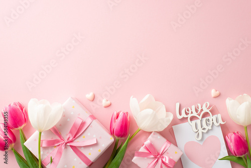 Mother's Day celebration concept. Top view photo of present boxes with bows pink white tulips envelope with postcard text love you and small hearts on isolated pastel pink background with copyspace