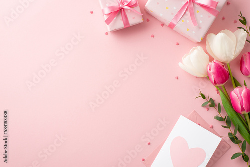 Mother's Day concept. Top view photo of gift boxes with ribbon bows bouquet of pink and white tulips envelope with postcard and heart shaped sprinkles on isolated pastel pink background with copyspace © ActionGP