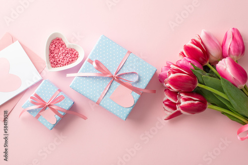 Mother's Day concept. Top view photo of blue gift boxes with ribbon bows bouquet of pink tulips heart shaped saucer with sprinkles and envelope with postcard on isolated pastel pink background © ActionGP