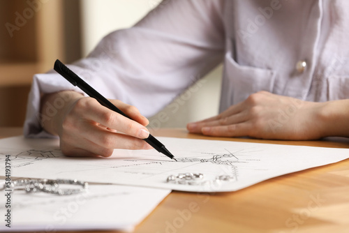 Jeweler drawing sketch of elegant necklace on paper at wooden table indoors, closeup photo