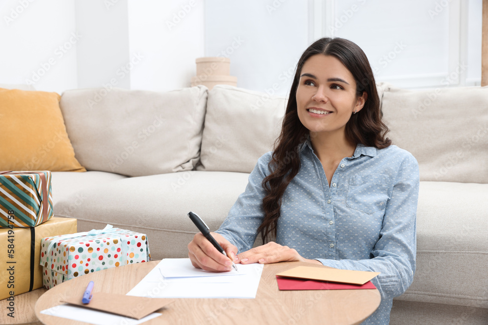 Young woman writing message in greeting card at table indoors Young woman writing message in greeting card at table indoors