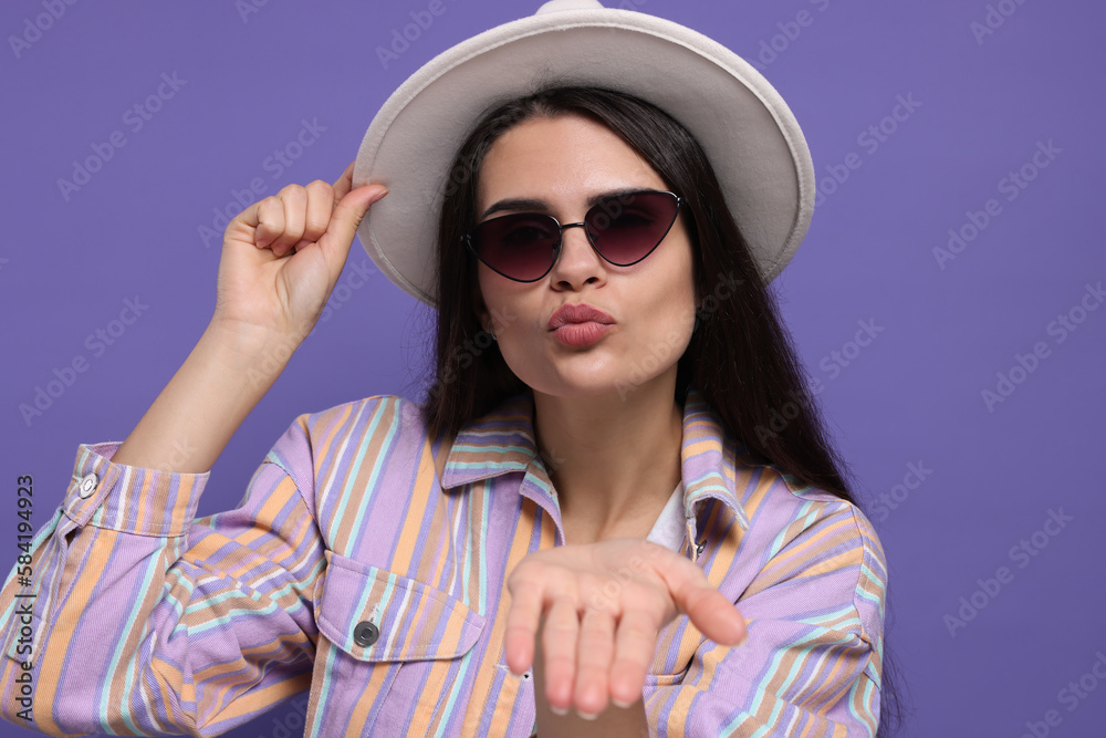 Beautiful young woman with stylish hat blowing kiss on purple background Beautiful young woman with stylish hat blowing kiss on purple background