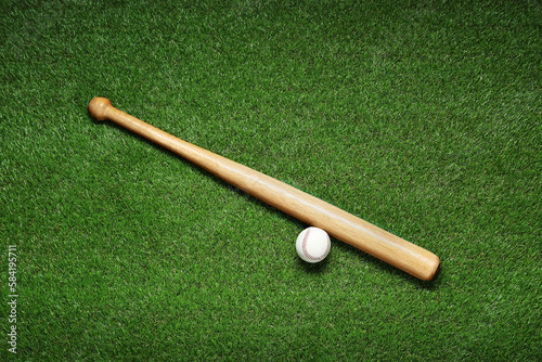 Wooden baseball bat and ball on green grass, flat lay. Sports equipment