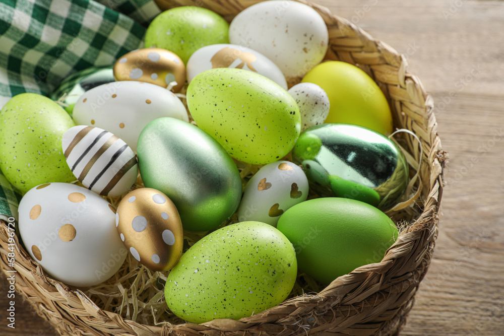 Many beautifully decorated Easter eggs in wicker basket on wooden table, closeup