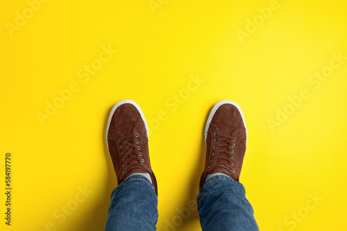 Man in stylish sneakers standing on yellow background, top view