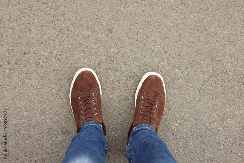 Man in stylish sneakers standing on asphalt, top view. Space for text