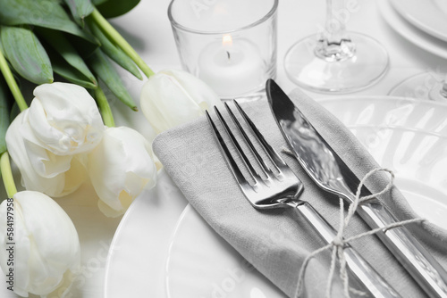 Stylish setting with cutlery, burning candle and tulips on white wooden table, closeup