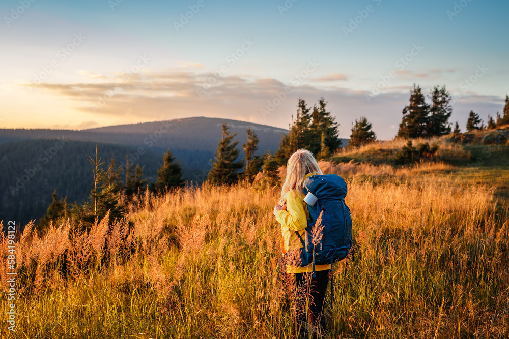 Woman with backpack looking at mountain range in natural parkland Jeseniky during sunset. Landscape with hiking tourist