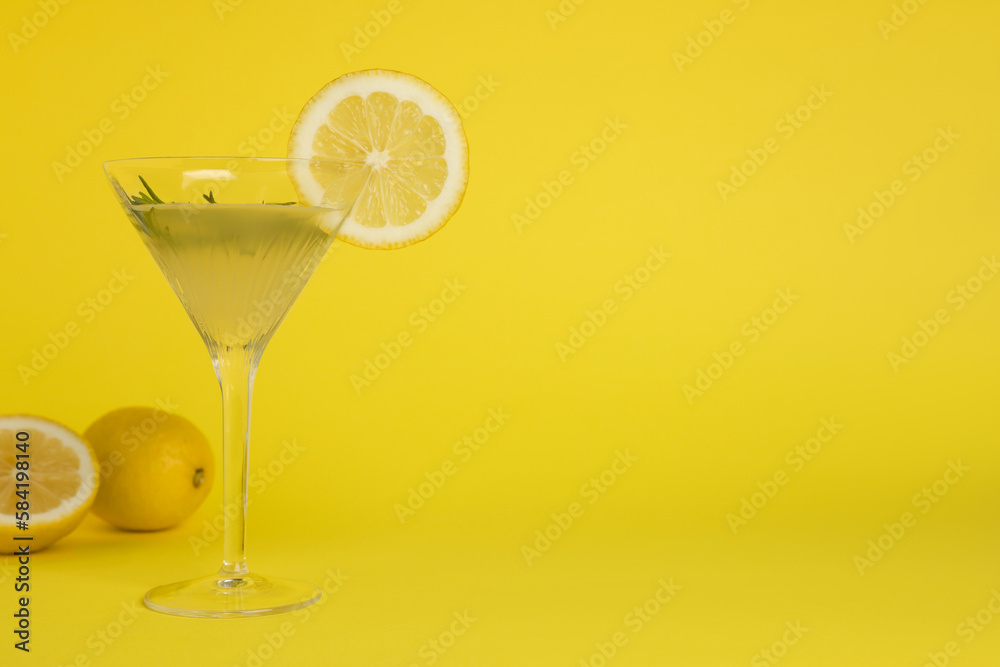 Martini glass of refreshing cocktail with lemon slice, rosemary and fruits on yellow background, space for text
