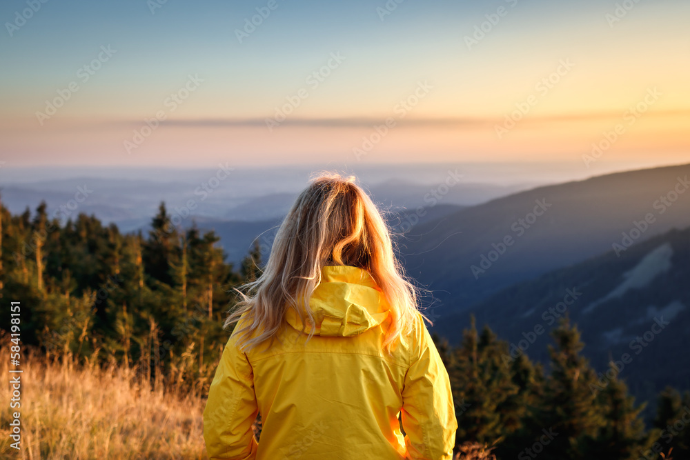 Woman with yellow jacket looking at mountain range during sunset. Hiking in mountains Woman with yellow jacket looking at mountain range during sunset. Hiking in mountains