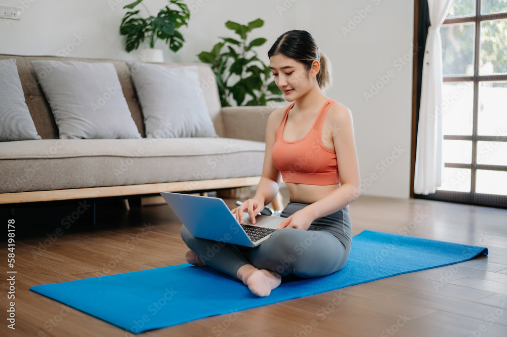 Asian Woman Doing Yoga and Watching Online Tutorials on Laptop, Training in Living Room Asian Woman Doing Yoga and Watching Online Tutorials on Laptop, Training in Living Room
