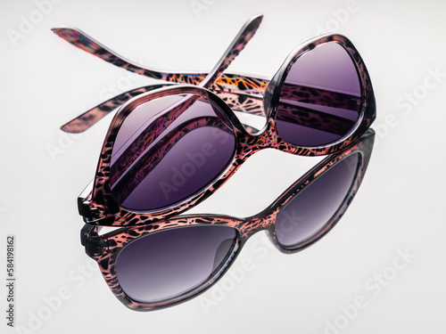 Female dark purple sunglasses with reflection isolated on light gray background. Horizontal. Nobody. Studio shot. Close-up.