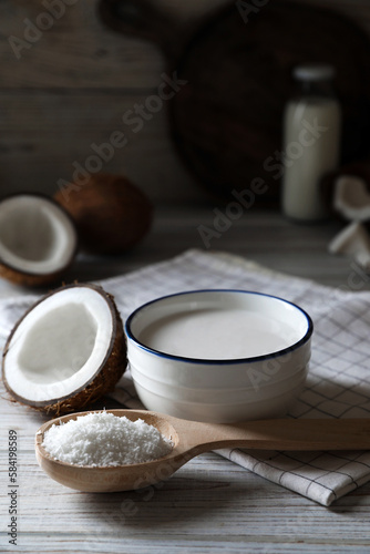 Bowl of delicious coconut milk, spoon with flakes and nuts on white wooden table, space for text