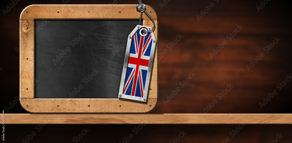 Empty blackboard with wooden frame and copy space, and a metal label with the UK flag (Union Jack Flag). On a wooden desk or shelf, front view. - obrazy, fototapety, plakaty 