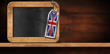 Empty blackboard with wooden frame and copy space, and a metal label with the UK flag (Union Jack Flag). On a wooden desk or shelf, front view.