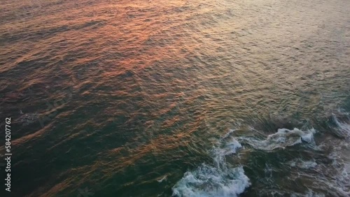 Aerial view from above on the beautiful surface of the sea and waves at sunset. Ocean coast. Calm beautiful video on the background for tourism, design and advertising