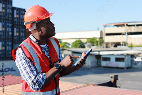Foreman using tablet and walkie talkie radio control loading containers box. Engineer or worker with safety hat work at container cargo site and checking industrial container cargo freight ship.