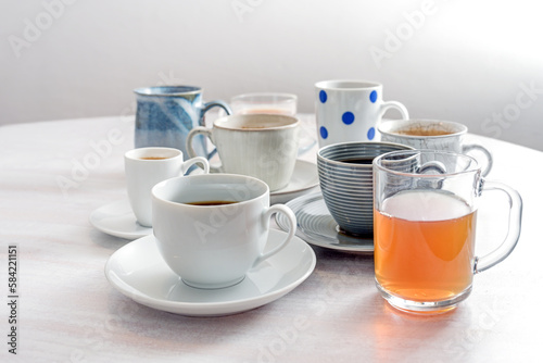 Tea and coffee cups in different styles on a white wooden table against a light gray wall  copy space  selected focus