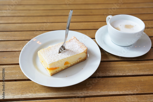 Piece of cheesecake with tangerines and icing sugar, a cake fork and a cup of coffee on a wooden table in the cafe, copy space, selected focus