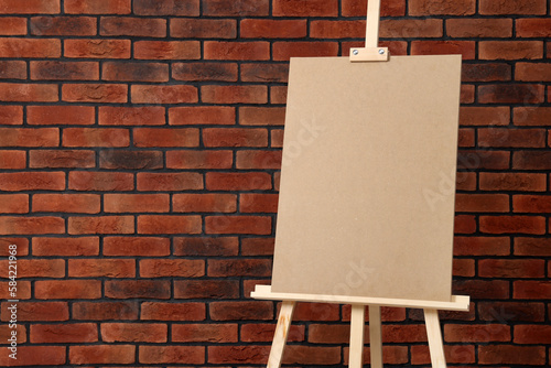 Wooden easel with blank board near brick wall, closeup. Space for text