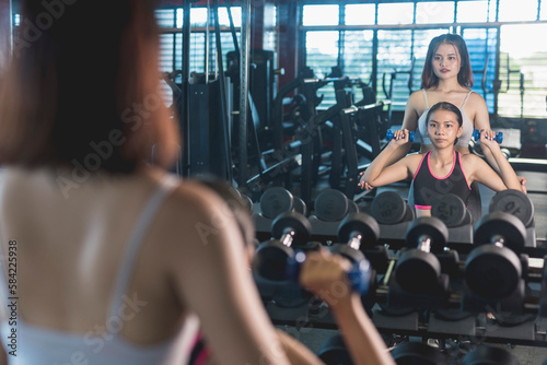A woman spots her friend doing seated dumbbell shoulder presses. Guiding and teaching how to properly workout. photo