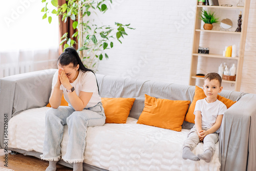 An exhausted young mother is sitting on the couch, tired of the bad behavior of a noisy child, a sick, irritated mother is resting on the couch, suffering from a headache, the concept of parenting