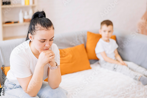 close-up of an exhausted young mother who is sitting on the couch, tired of the bad behavior of a noisy child, parenting concept