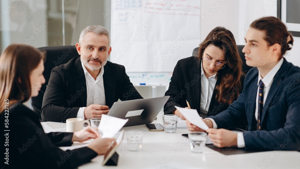 Focused businesspeople discuss documents. Group of business partners reading contract agreement in the meeting room Focused businesspeople discuss documents. Group of business partners reading contract agreement in the meeting room