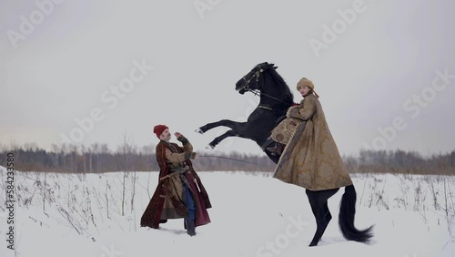 ancient european queen on black horse and groom in winter landscape, historical reconstruction photo