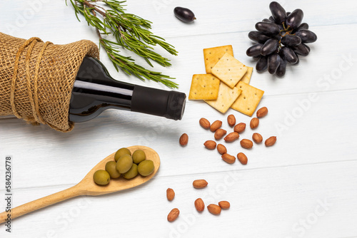 Green olives in wooden spoon. Nuts, crackers and sprig of black grapes on table.
